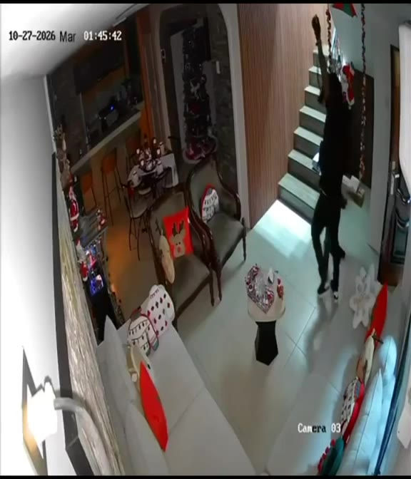 Cámara de seguridad dentro de una casa: un hombre vestido de negro sube una escalera.