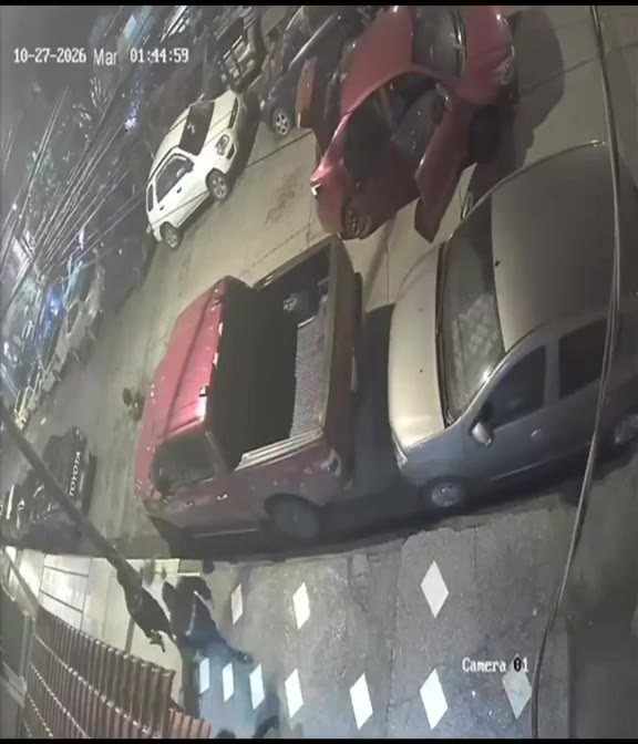 Cámara de seguridad desde lo alto: una calle de noche con autos estacionados, entre ellos una camioneta roja.