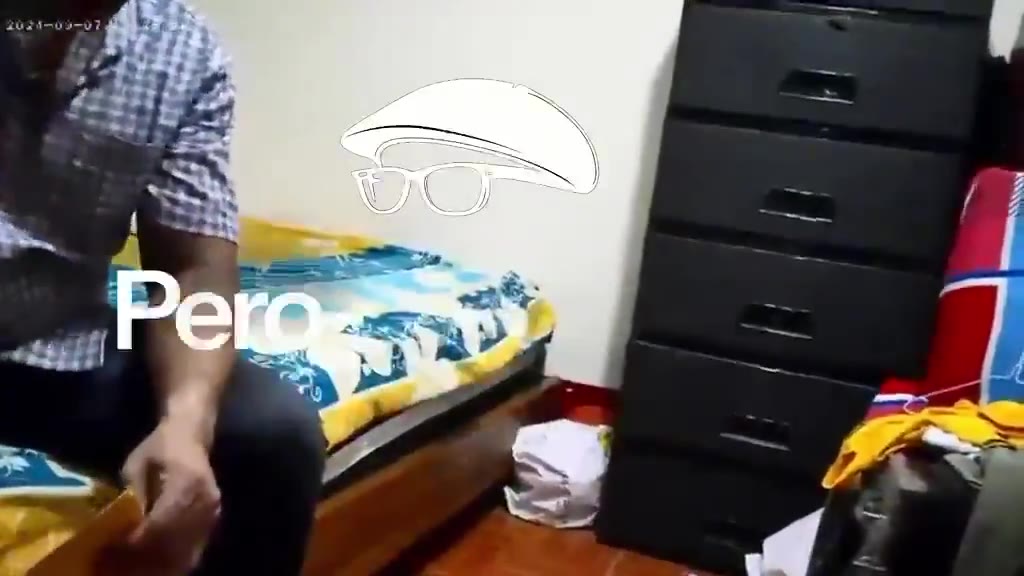 Fotograma de la grabación: un hombre con camisa a cuadros sentado en una cama, con subtítulo sobreimpreso.