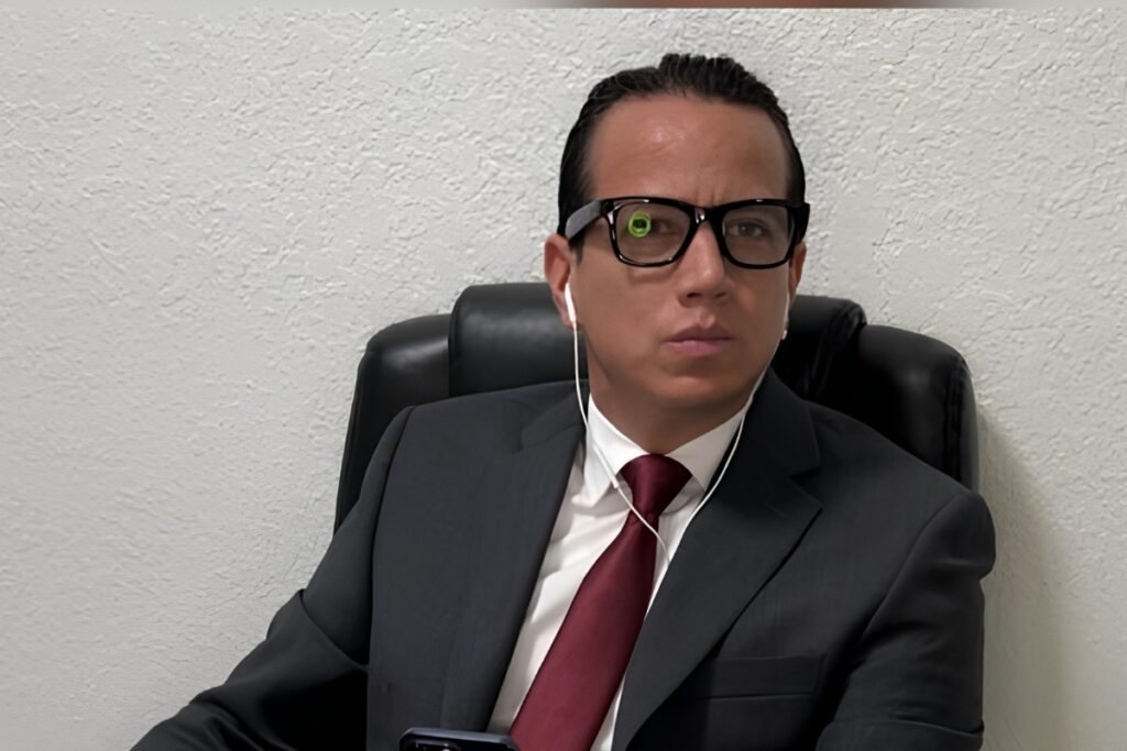 Leonardo Toledo, de traje oscuro, corbata roja y lentes, sentado en un sillón de oficina.